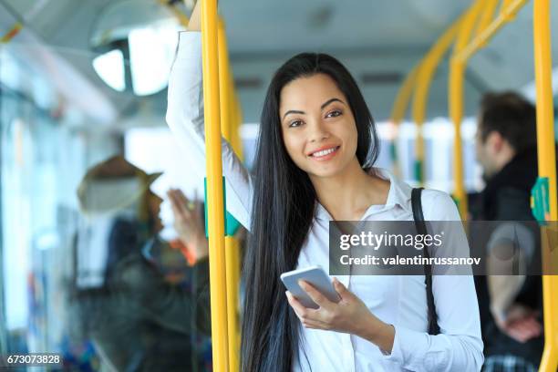 cheerful young woman traveling and using smart phone - crowded public transport stock pictures, royalty-free photos & images