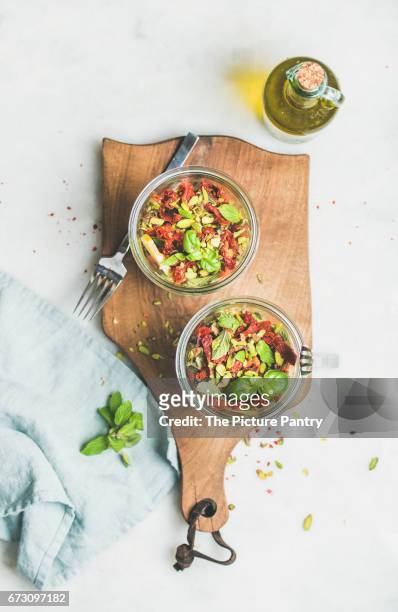 healthy vegan energy boosting salad with quionoa, avocado, dried tomatoes, basil, olive oil, mint in glass jars, marble background, top view - avocato oil stock pictures, royalty-free photos & images