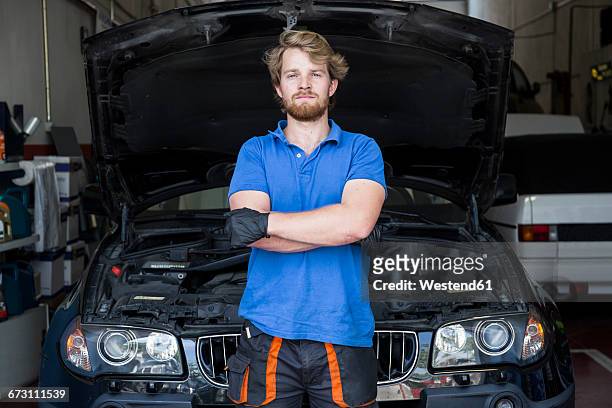 mechanic standing in his car workshop with arms crossed - three quarter length fotografías e imágenes de stock