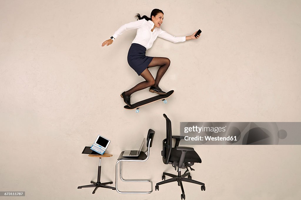 Businesswoman skateboarding over office chairs with smartphone