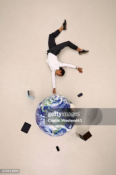 businesswoman balancing on fingertip on globe with mobile devices - businesswoman handstand stock pictures, royalty-free photos & images