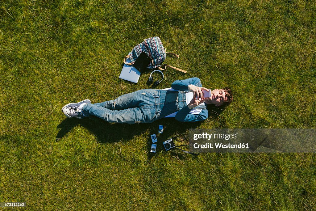 Relaxed young man lying on a meadow using cell phone, top view