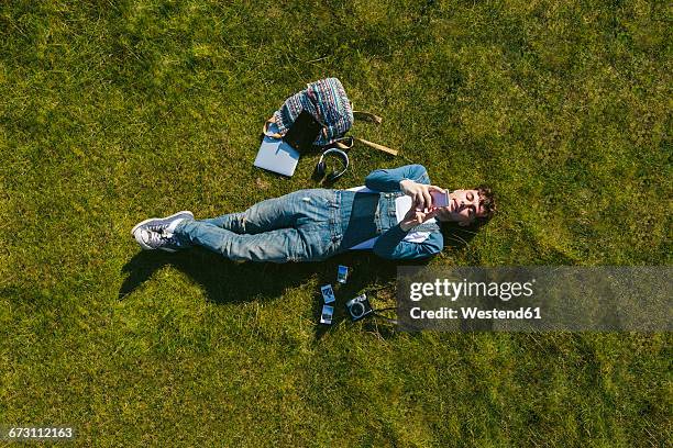 relaxed young man lying on a meadow using cell phone, top view - im gras liegen stock-fotos und bilder