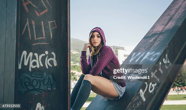 young woman wearing hooded jacket and stockings sitting on pillar - graffiti hintergrund stock pictures, royalty-free photos & images