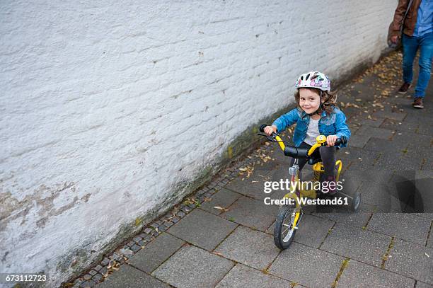 daughter riding bicycle with training wheels - stützrad stock-fotos und bilder