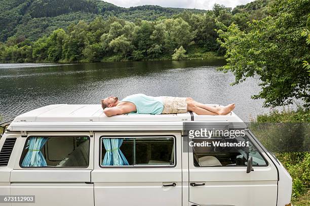man lying on roof of a van at lakeside - indulgence stock pictures, royalty-free photos & images