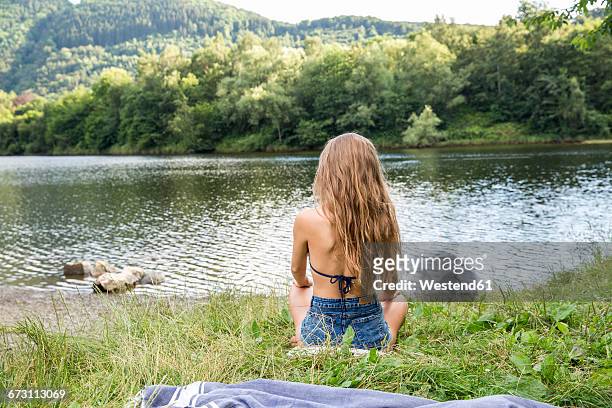 young woman sitting at lakeside - riva del lago foto e immagini stock