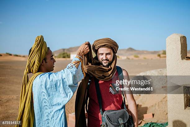 berber guide helping touist wrapping a turban - merzouga stock pictures, royalty-free photos & images