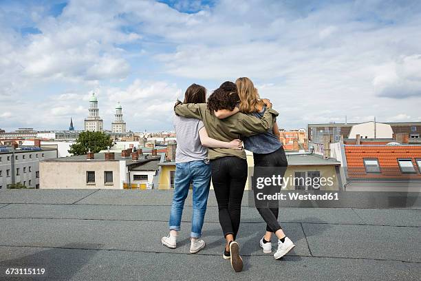 germany, berlin, back view of three teenage girls standing arm in arm on roof top - arms around stockfoto's en -beelden