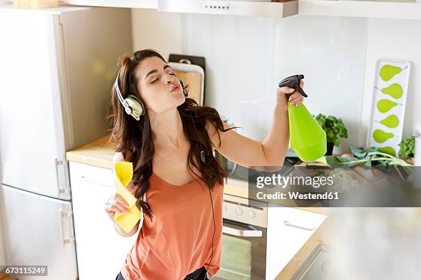 young woman in kitchen cleaning and listening to music - spray bottle stock pictures, royalty-free photos & images