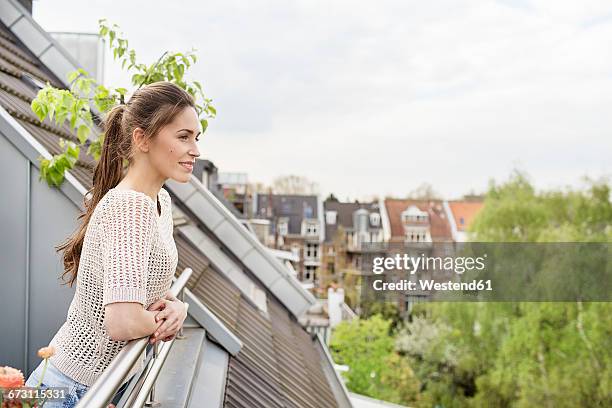 smiling young woman standing on balcony - balcony fotografías e imágenes de stock