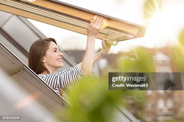 smiling young woman cleaning roof window - frau putzen stock-fotos und bilder