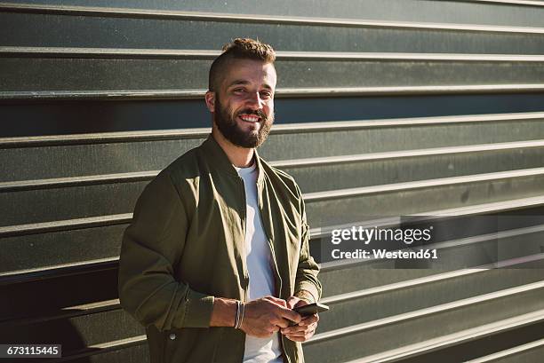 portrait of smiling man with cell phone standing in front of facade - pompadour stock pictures, royalty-free photos & images