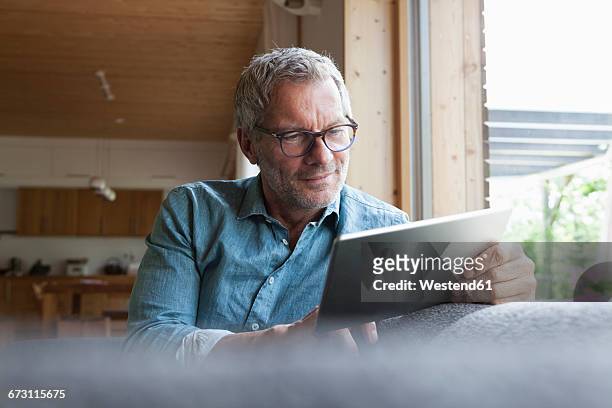 mature man using digital tablet on couch - tablet pc stock-fotos und bilder