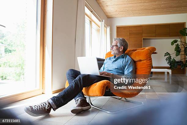 mature man using laptop in armchair - man using laptop fotografías e imágenes de stock