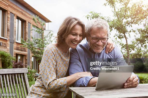 happy mature couple sharing digital tablet in garden - couple at table with ipad stockfoto's en -beelden