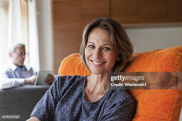 smiling woman relaxing in armchair with husband in background - 45 couple stockfoto's en -beelden