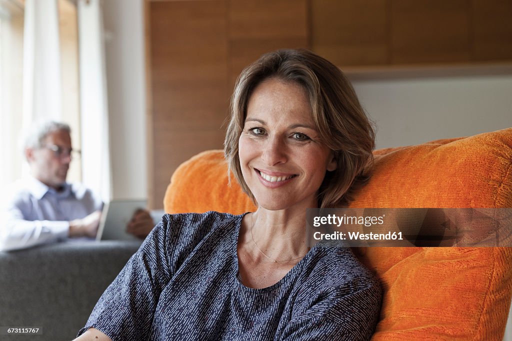 Smiling woman relaxing in armchair with husband in background