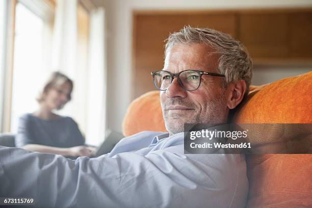 man relaxing in armchair with wife in background - differential focus stock pictures, royalty-free photos & images