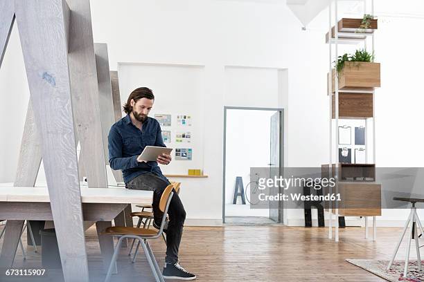 man sitting on office desk using digital tablet - emanzipation stock-fotos und bilder