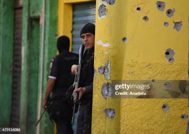 Police officer stands near a wall, which has bullet holes on, as he looks for drug traffickers in Favela do Alemao, north of Rio de Janeiro, Brazil...
