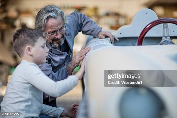 senior man and boy examining old car together - oldtimerauto stockfoto's en -beelden