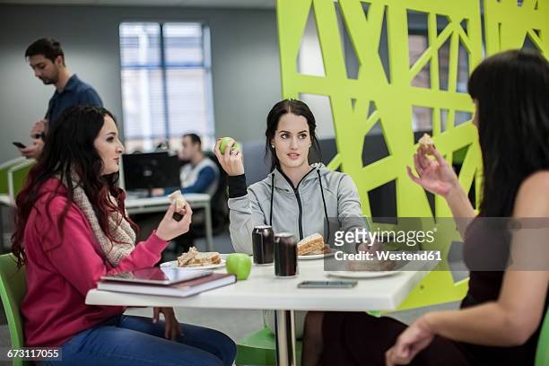 three women discussing in office canteen - staples office stockfoto's en -beelden