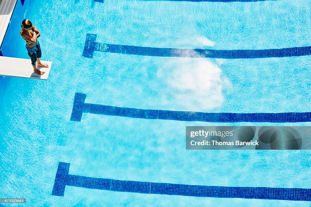 Young boy standing at end of diving board at pool