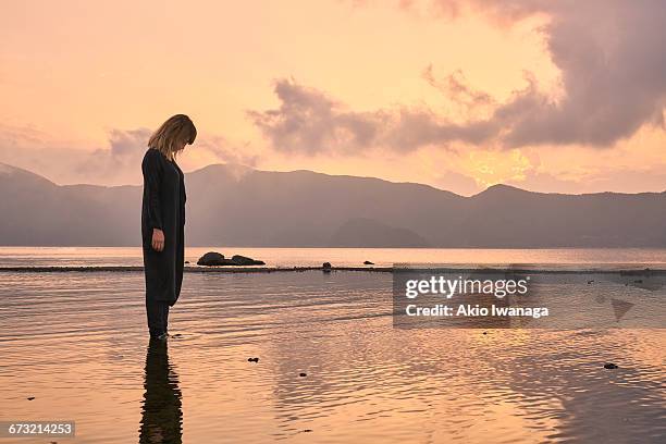 woman standing in the lake of the sunset - akio iwanaga stock pictures, royalty-free photos & images