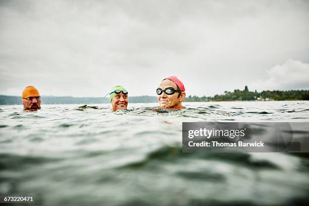 smiling swimmers resting during open water swim - schwimmen wettkampf stock-fotos und bilder