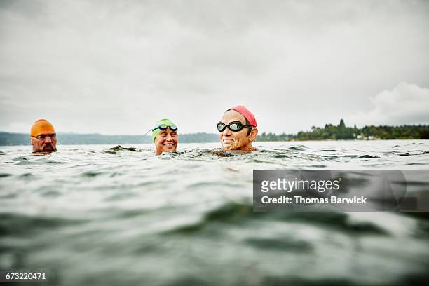 smiling swimmers resting during open water swim - 50 59 years stock pictures, royalty-free photos & images