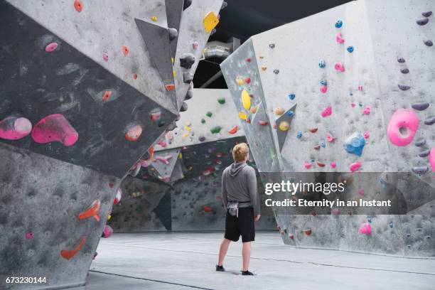 young man looking up at climbing wall before climbing - rock climbing stock pictures, royalty-free photos & images