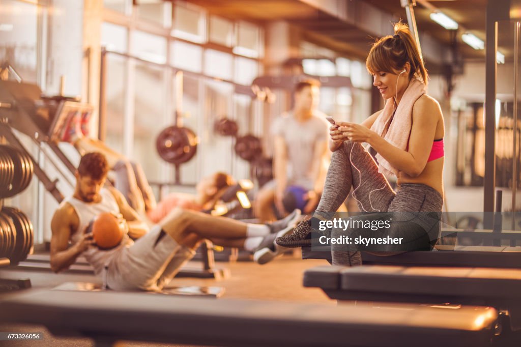 Smiling woman enjoying in music over earphones in a gym.