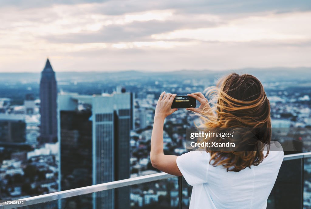 Woman taking photo with mobile phone above city