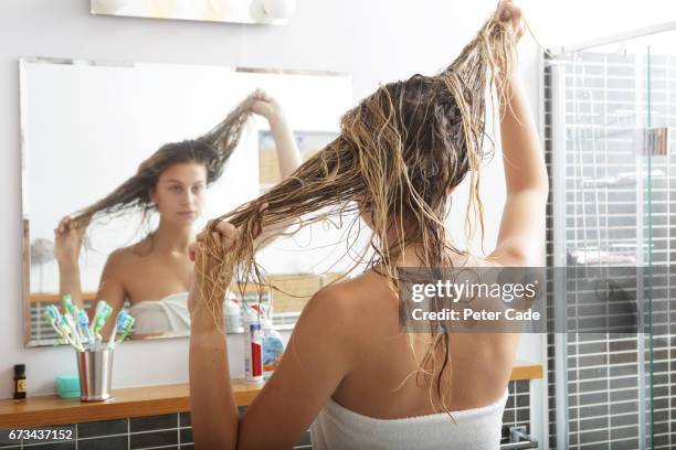 young woman looking in mirror at wet hair - haare waschen stock-fotos und bilder