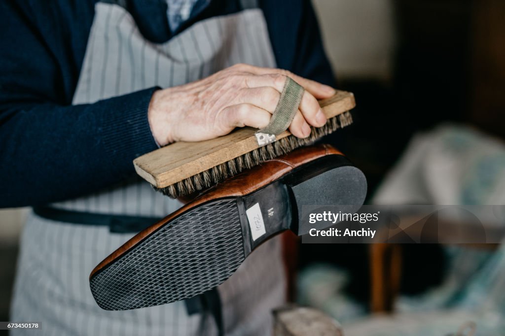 Old shoemaker is polishing a shoe