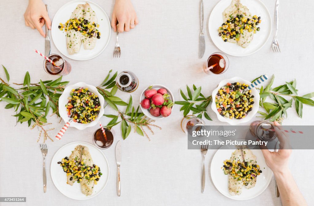 A summery (happy & bright) tablesetting with a portion of Baked Lime and Olive oil tilapia with black bean salsa served on each plate. (only glasses)