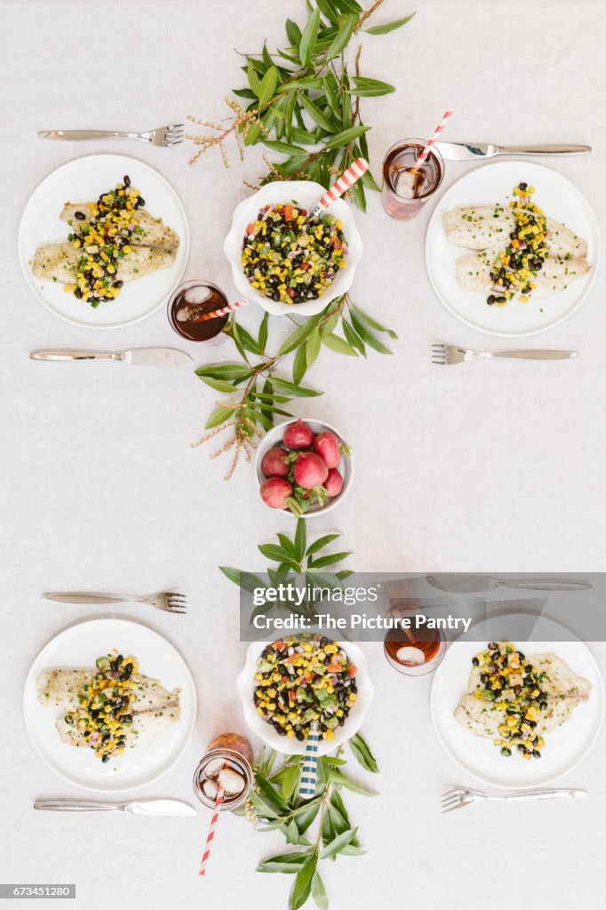 A summery (happy & bright) tablesetting with a portion of Baked Lime and Olive oil tilapia with black bean salsa served on each plate.