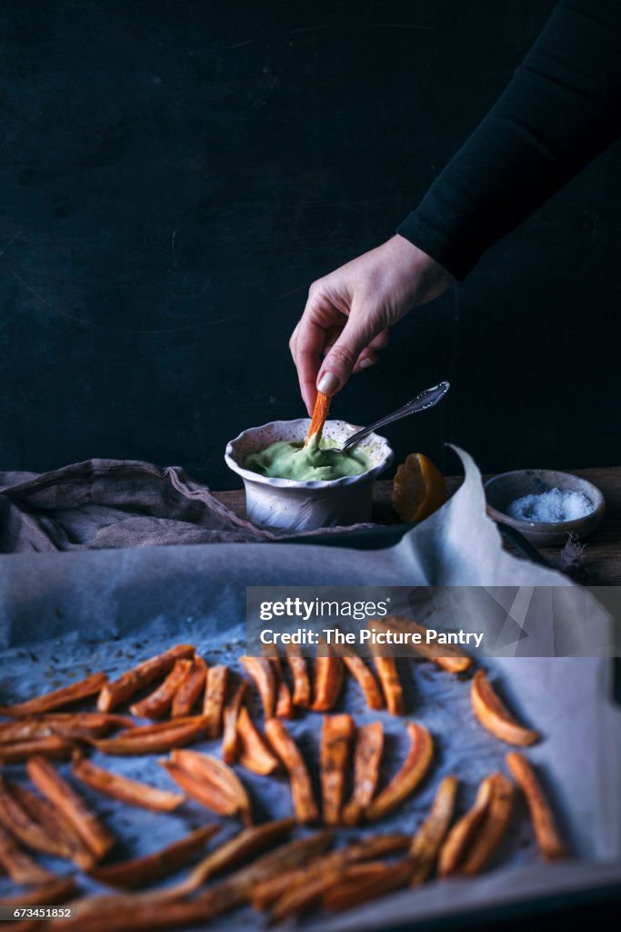 Woman dipping oven baked sweet potatoe fries into avocado sauce