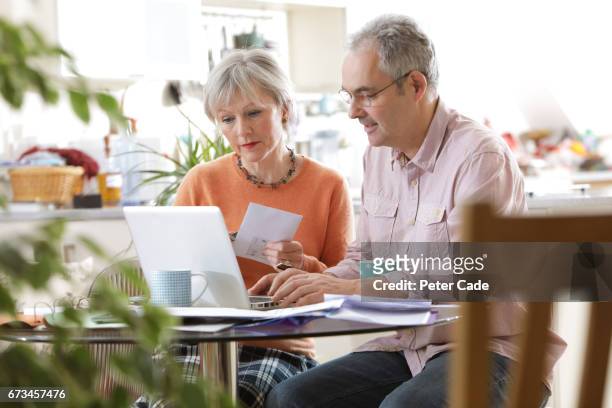 older couple sat at home looking at laptop - mann am tisch mit papier stock-fotos und bilder