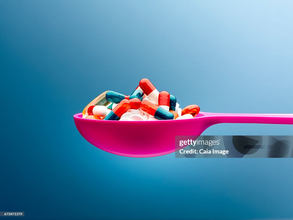 Medicine capsules in pink spoon against blue background