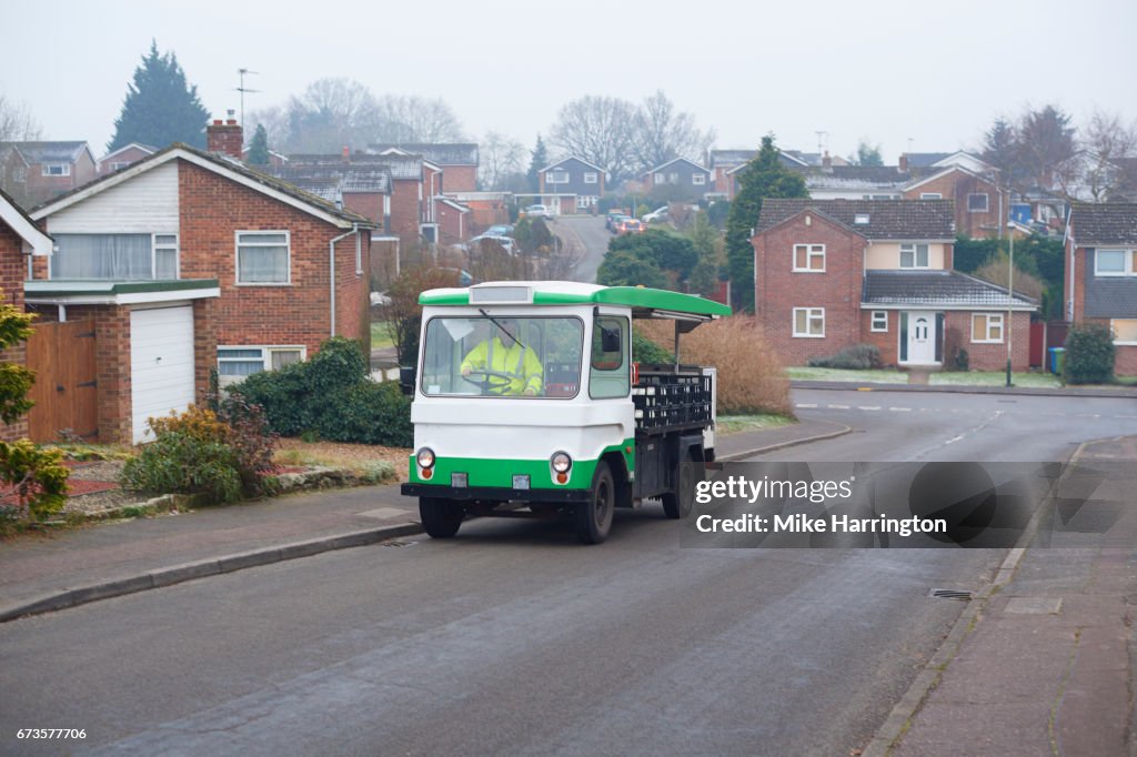 Milkman driving his milk float up an urban street