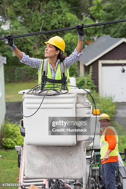 hispanic female cable lineman examining the cables in the rain - cherry picker stock pictures, royalty-free photos & images