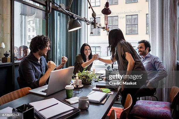 happy businesswomen holding hands in meeting at creative office - aufregung stock-fotos und bilder