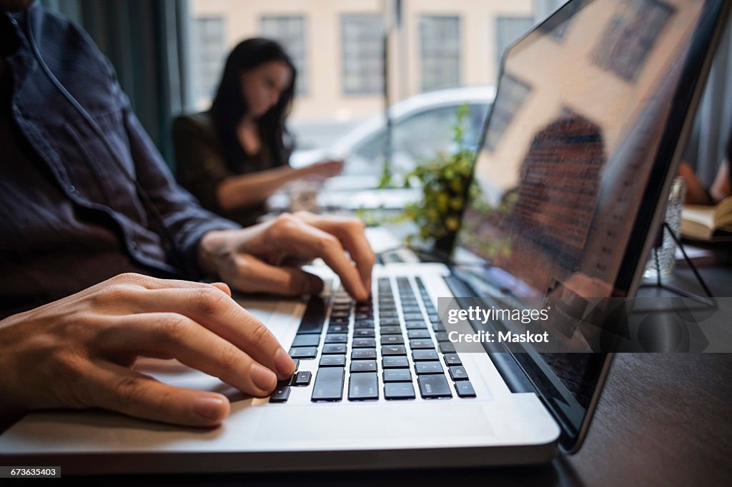 Close-up of businessman using laptop with colleague sitting at table in office