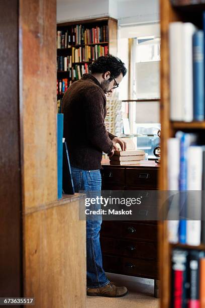 man reading book while standing seen from shelves - antique shop stock pictures, royalty-free photos & images