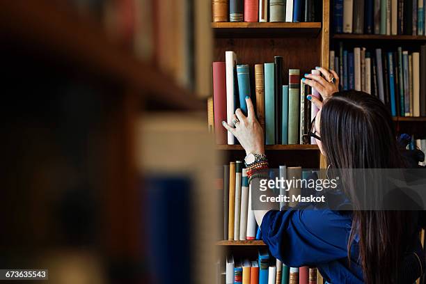 rear view of woman searching book in library - books on shelf stockfoto's en -beelden