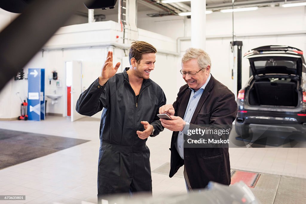 Happy mechanic with senior man using mobile app at auto repair shop