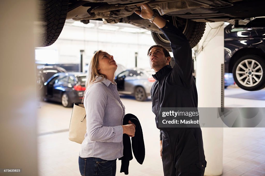 Male expert with client standing under car at repair shop