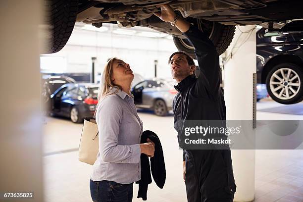 male expert with client standing under car at repair shop - autowerkstatt gegenlicht stock-fotos und bilder